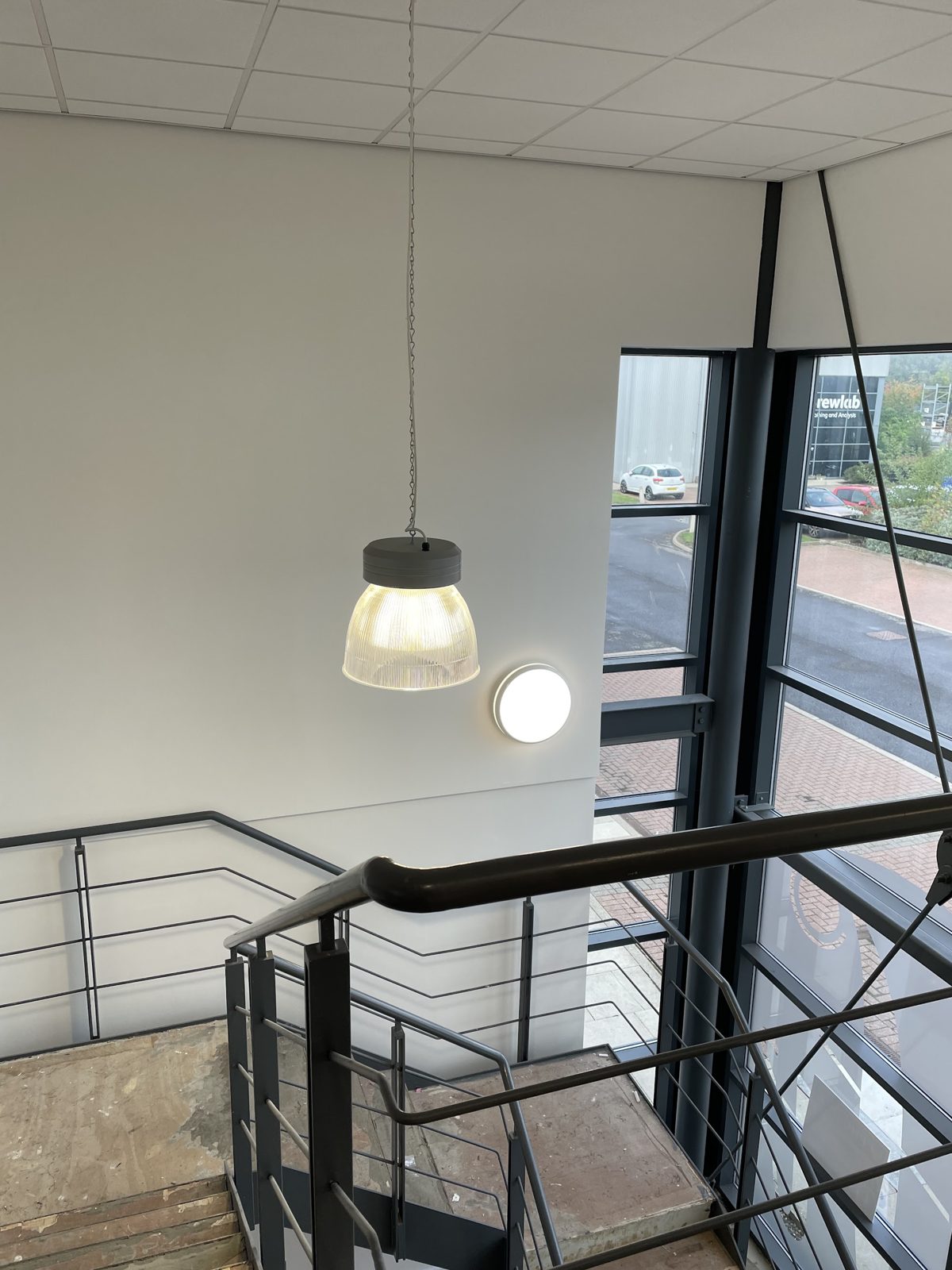 A glass pendant over a modern staircase beside a tall glazed wall