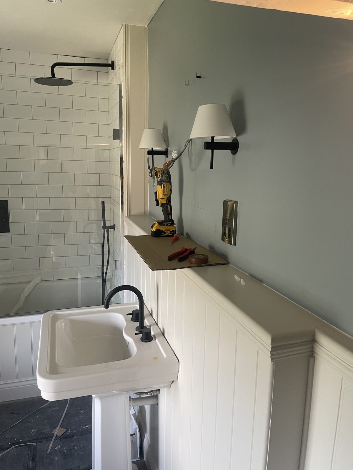 A bathroom with white wall lights above a pedestal basin and panelled walls