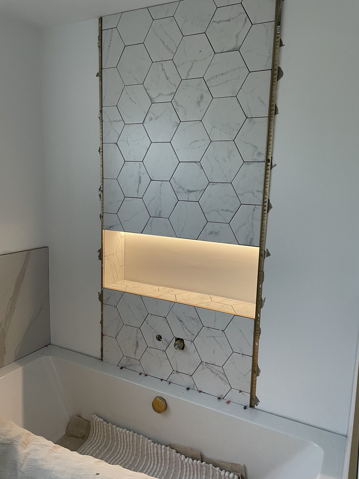 A recessed bathroom niche lit with warm LED strip, set into hexagonal marble-effect tiles